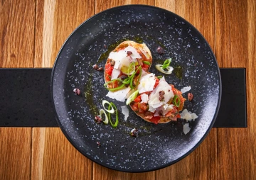 Burrata with tomatoes and herbs on a black plate, seen from above.