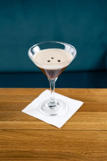Espresso Martini v koktejlové sklence na dřevěném stole.