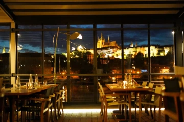 Interiér Marina Ristorante za soumraku s prostřenými stoly a výhledem na Pražský hrad.