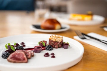 Tender meat with tartare and blackberries on a white plate.