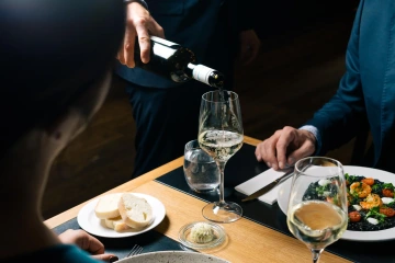 Server pouring white wine for guests at the table.