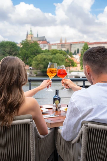 Pár si připíjí koktejly na terase Marina Ristorante s výhledem na Pražský hrad.