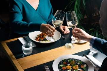 Couple dining on squid-ink risotto and toasting with white wine.