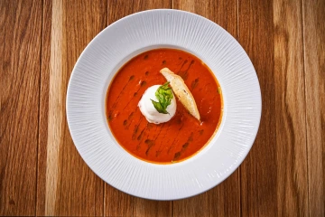 Tomato soup with cream and bread on a white plate.