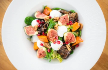 Salad with figs, mozzarella and pomegranate on a white plate.