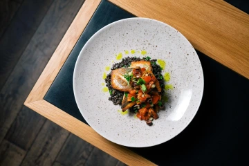 Na talíři s jemným dekorem se snoubí opečená ryba s čočkou a čerstvou salsou. Moderní gastronomie s důrazem na detail.