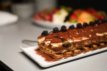 Tiramisu with blackberries on a rectangular plate.