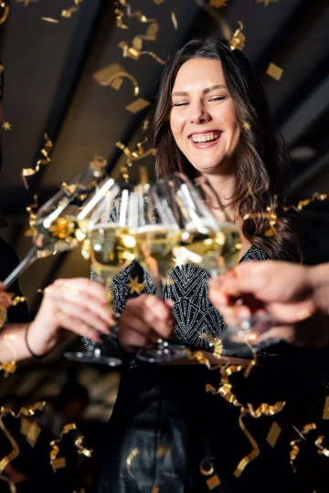 Woman with a glass of sparkling wine and golden confetti at a New Year's celebration.